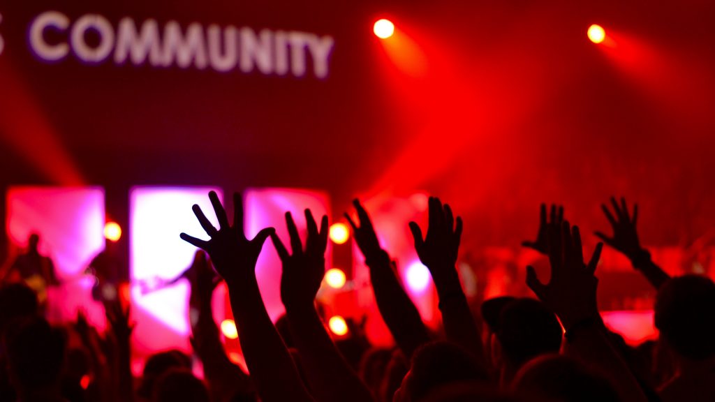 Hands raised in air with red background. The word community is blurred in background.